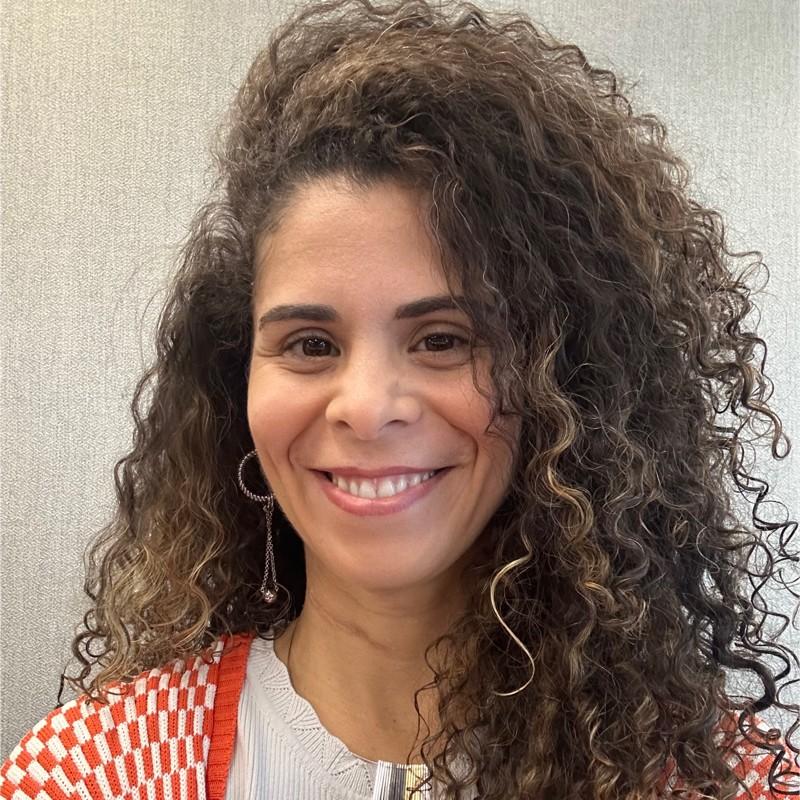 Luana Roncaratti. Mulher parda, com cabelos longos e encaracolados. 